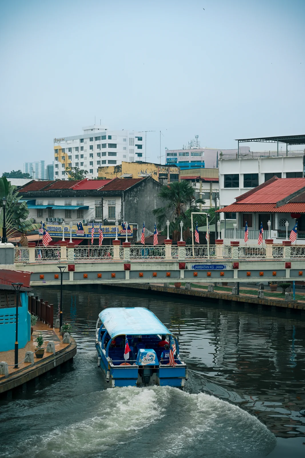 Daytime Malacca River cruise boat gliding past restored heritage shophouses