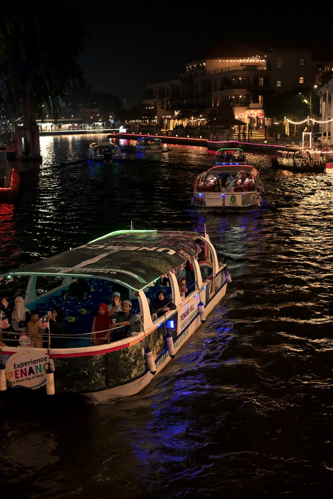 River cruise boat filled with passengers sailing under neon bridge lights