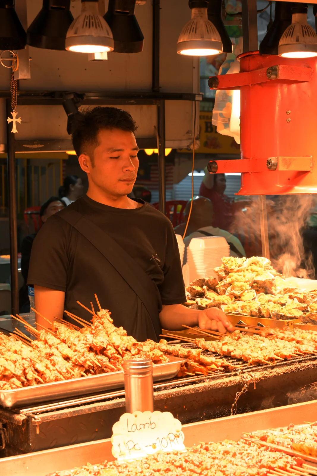 Jonker Walk night market vendor flipping skewers over glowing embers