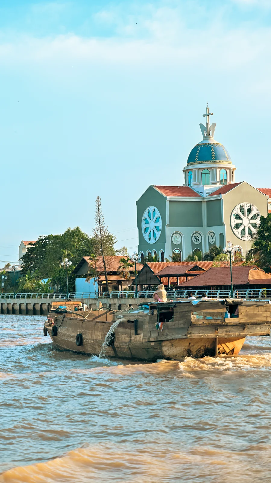 Wooden riverboat cruising past the blue tiled dome of Mỹ Tho Cathedral