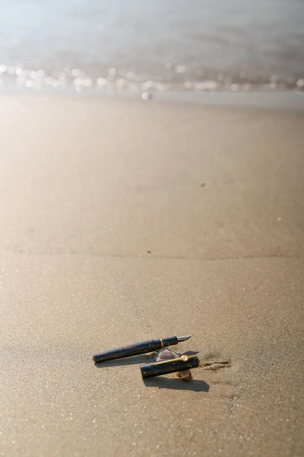 Fountain pen resting on wet shoreline sand with gentle foam waves washing ashore at Quy Nhơn