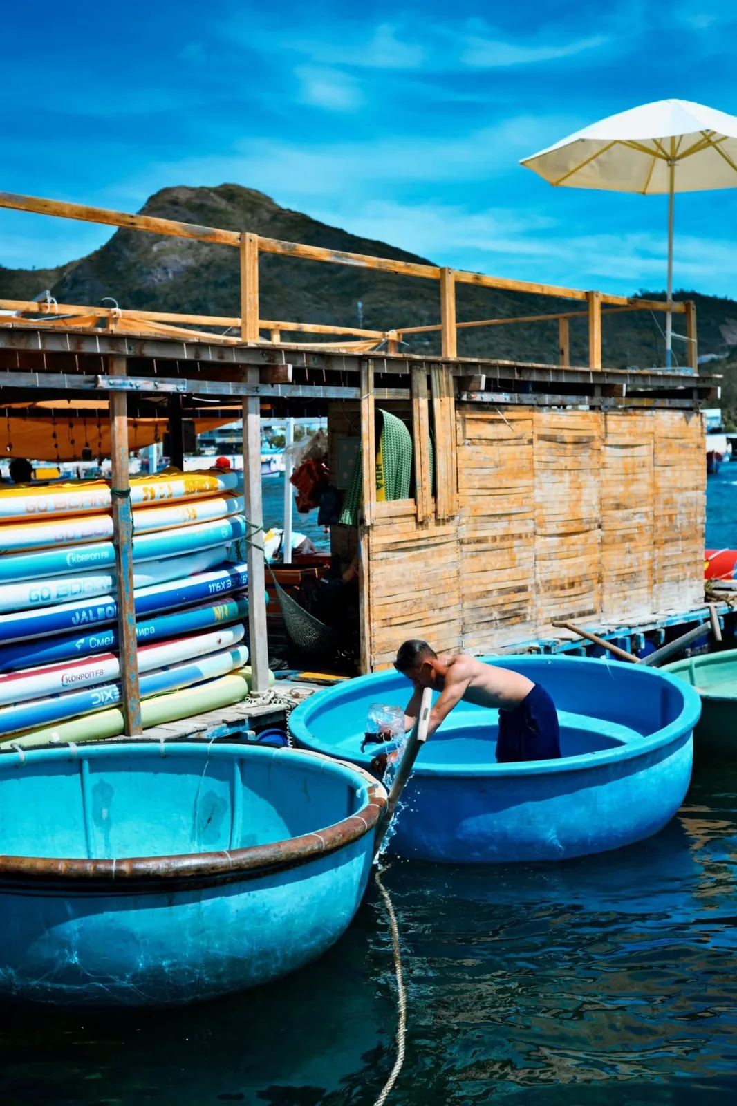 Blue basket boats and colorful paddleboards resting on a floating raft house in Quy Nhơn bay
