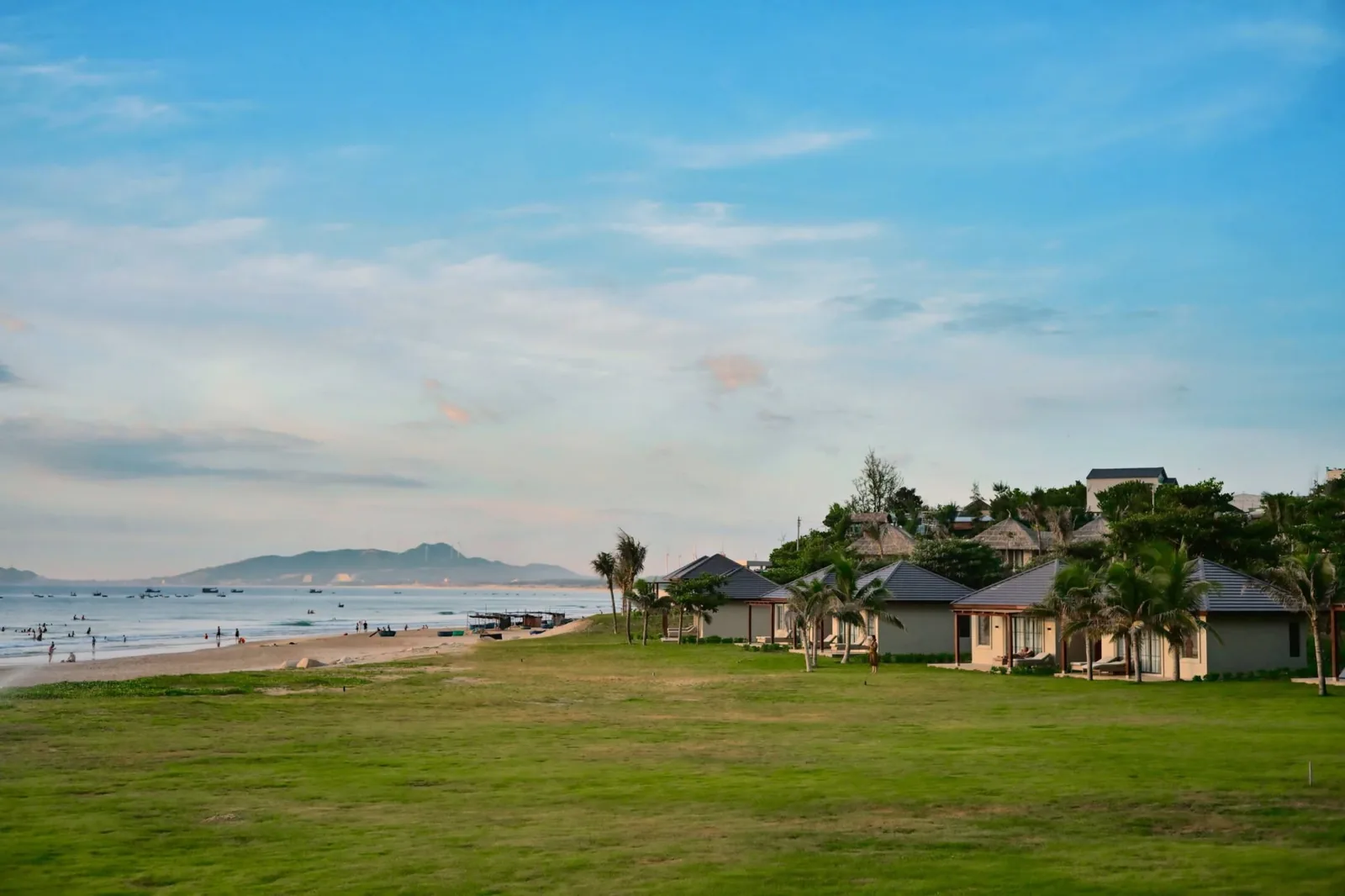 Beachfront resort villas and manicured green lawn facing the ocean surf and rocky headlands of Quy Nhơn