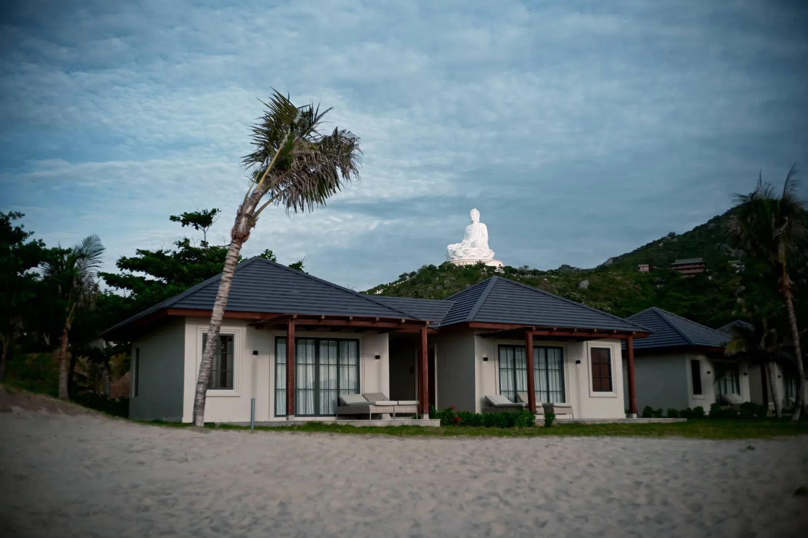 Resort villas flanked by palm trees with the giant Linh Phong Buddha statue watching over the mountain ridge in Quy Nhơn