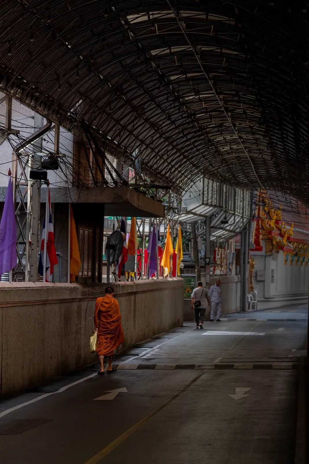 Buddhist monk walking along a covered passageway adorned with Thai flags