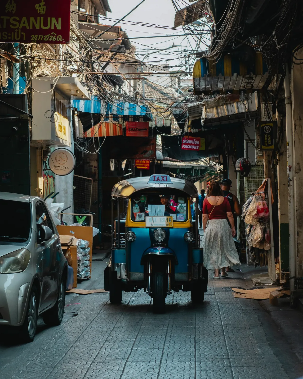Iconic blue Tuk-Tuk navigating a bustling narrow Bangkok alley under overhead wiring