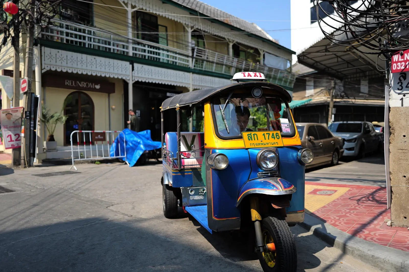 Classic yellow and blue Bangkok Tuk-Tuk parked beside traditional shophouses