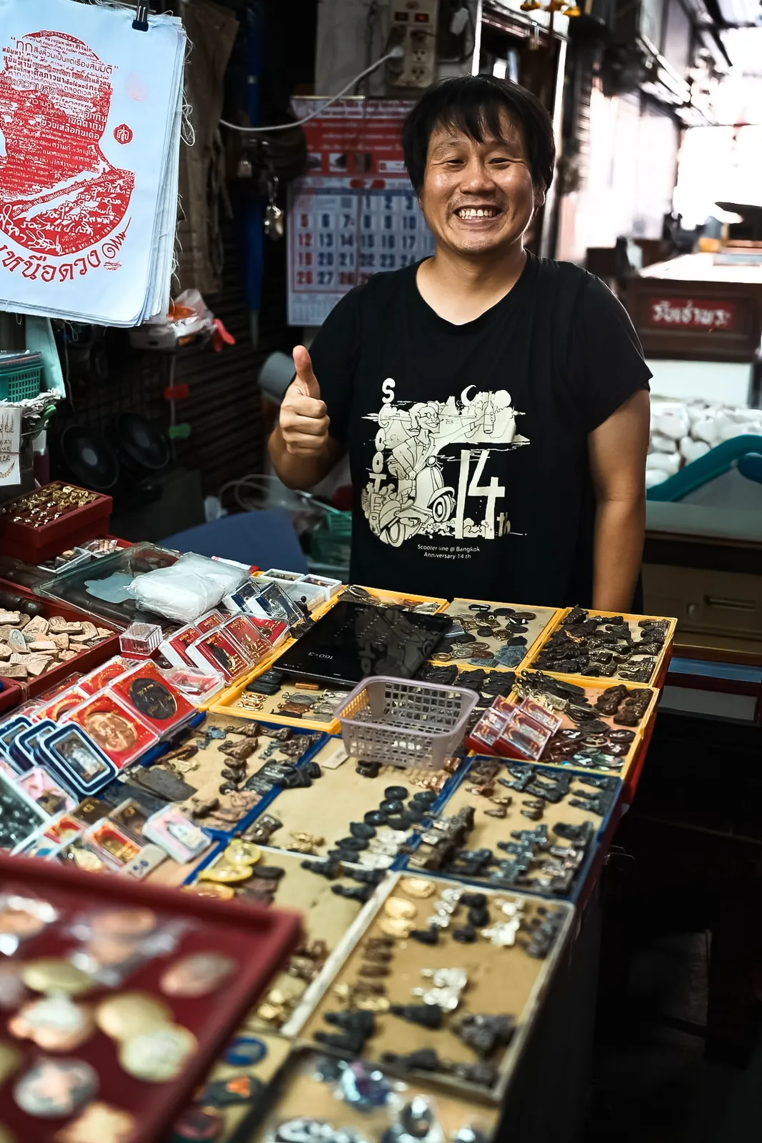 Friendly amulet market vendor giving a warm thumbs-up behind his collection