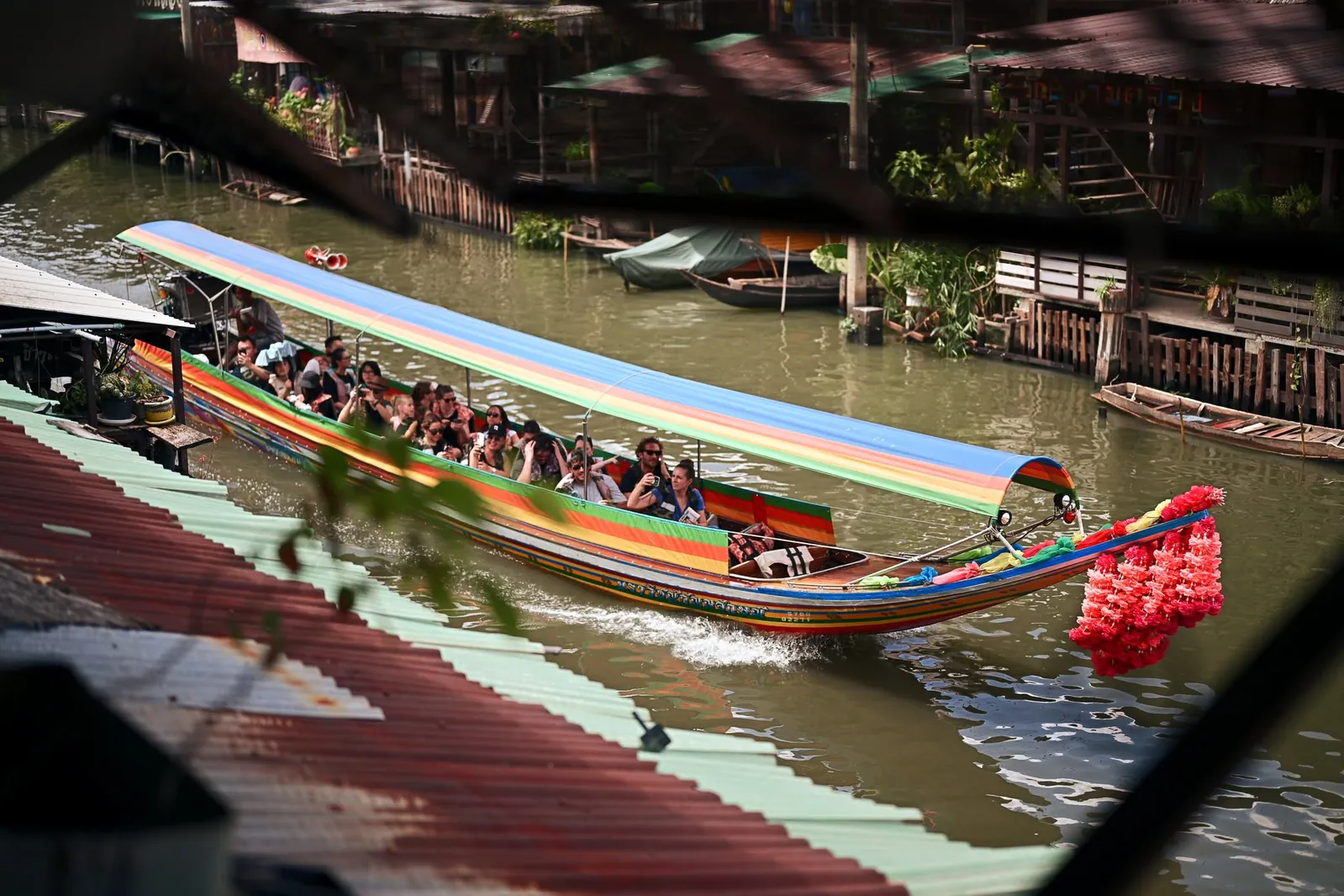 Long-tail boat with vibrant rainbow canopy cruising through Bangkok canal