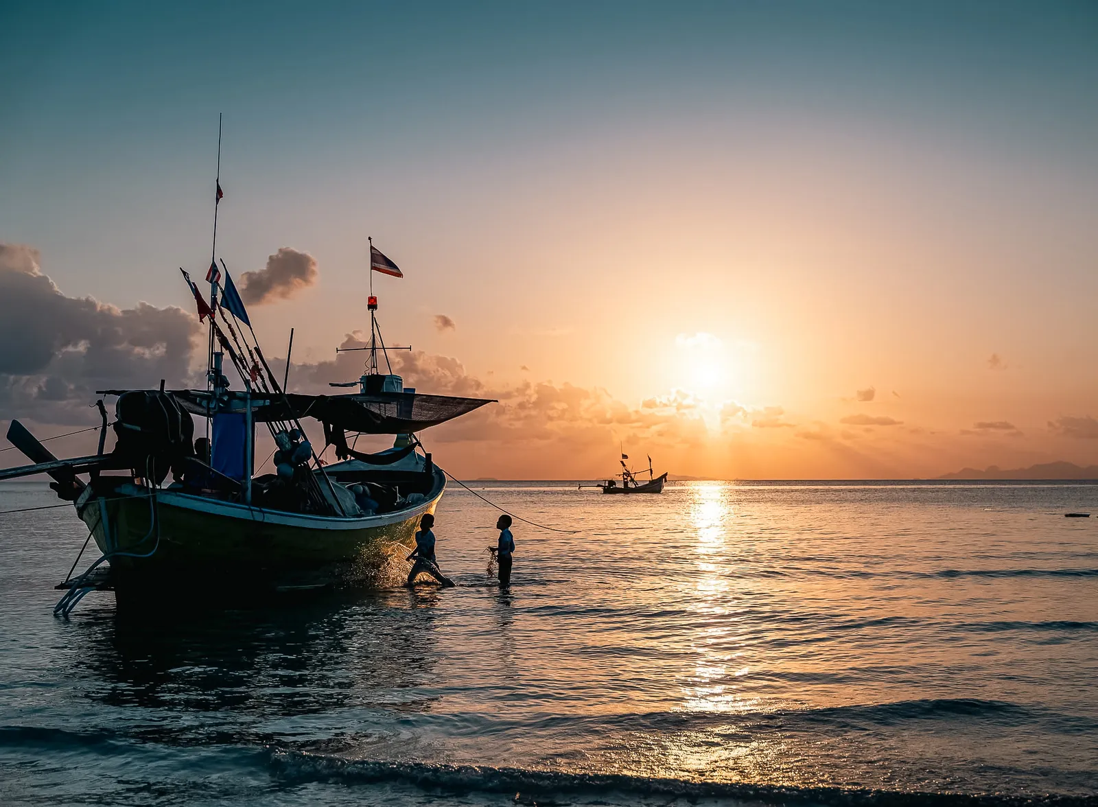 Sunset over calm sea with traditional wooden fishing boat flying the Thai flag