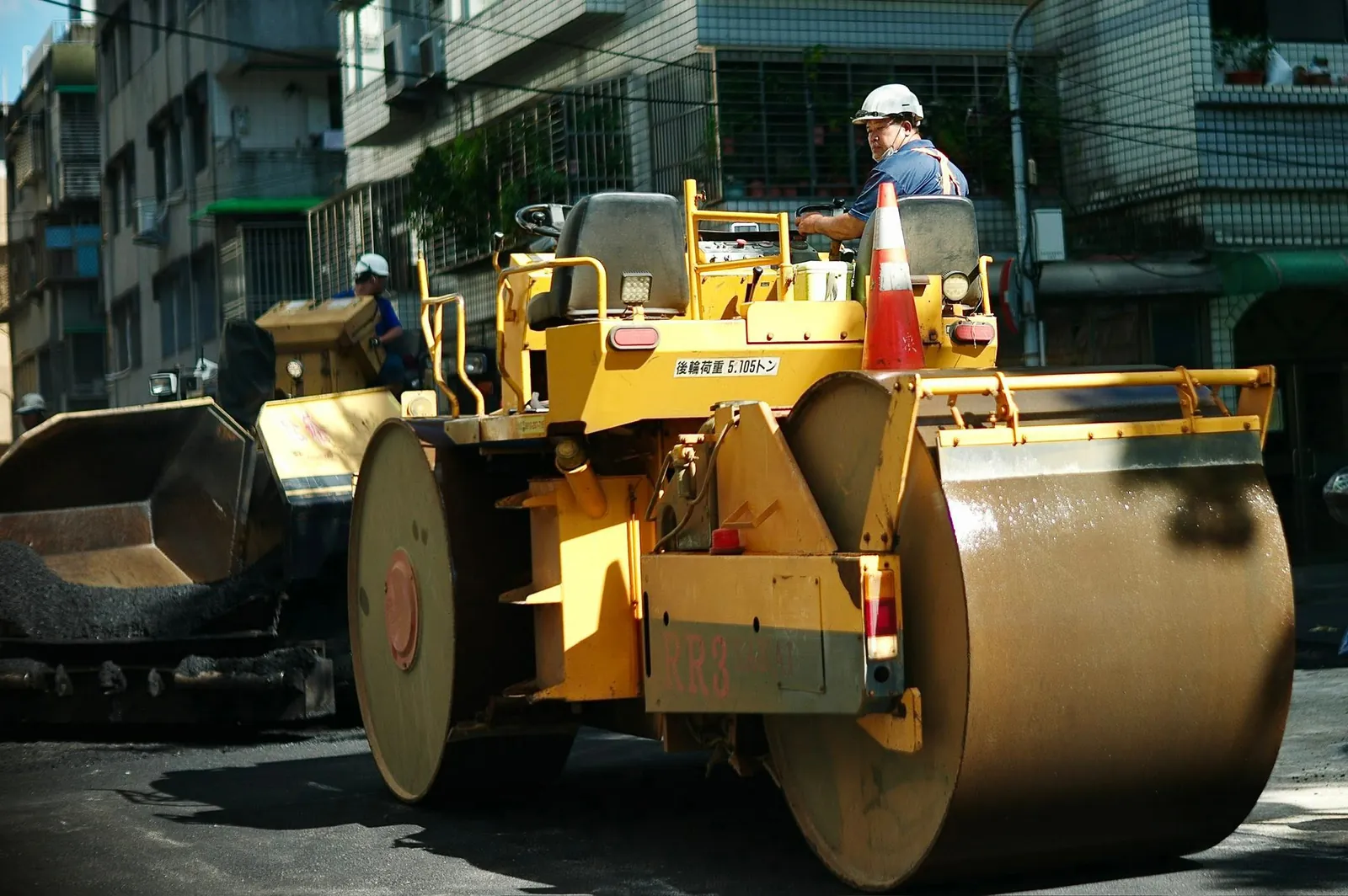 Street construction worker operating a yellow road roller compactor on urban asphalt